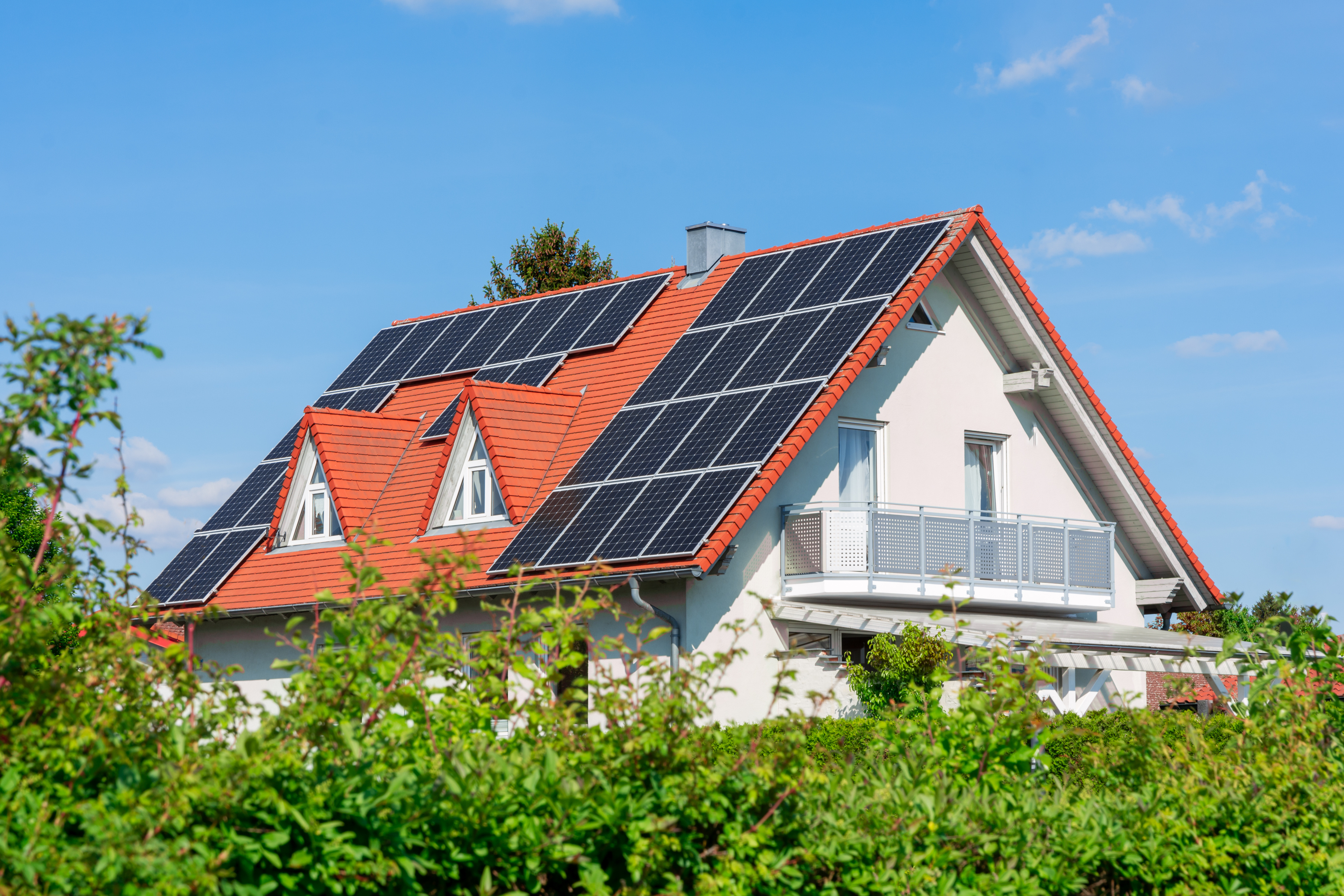 Das Bild zeigt ein Haus mit einem roten Satteldach, das mit Solarpanels ausgestattet ist.