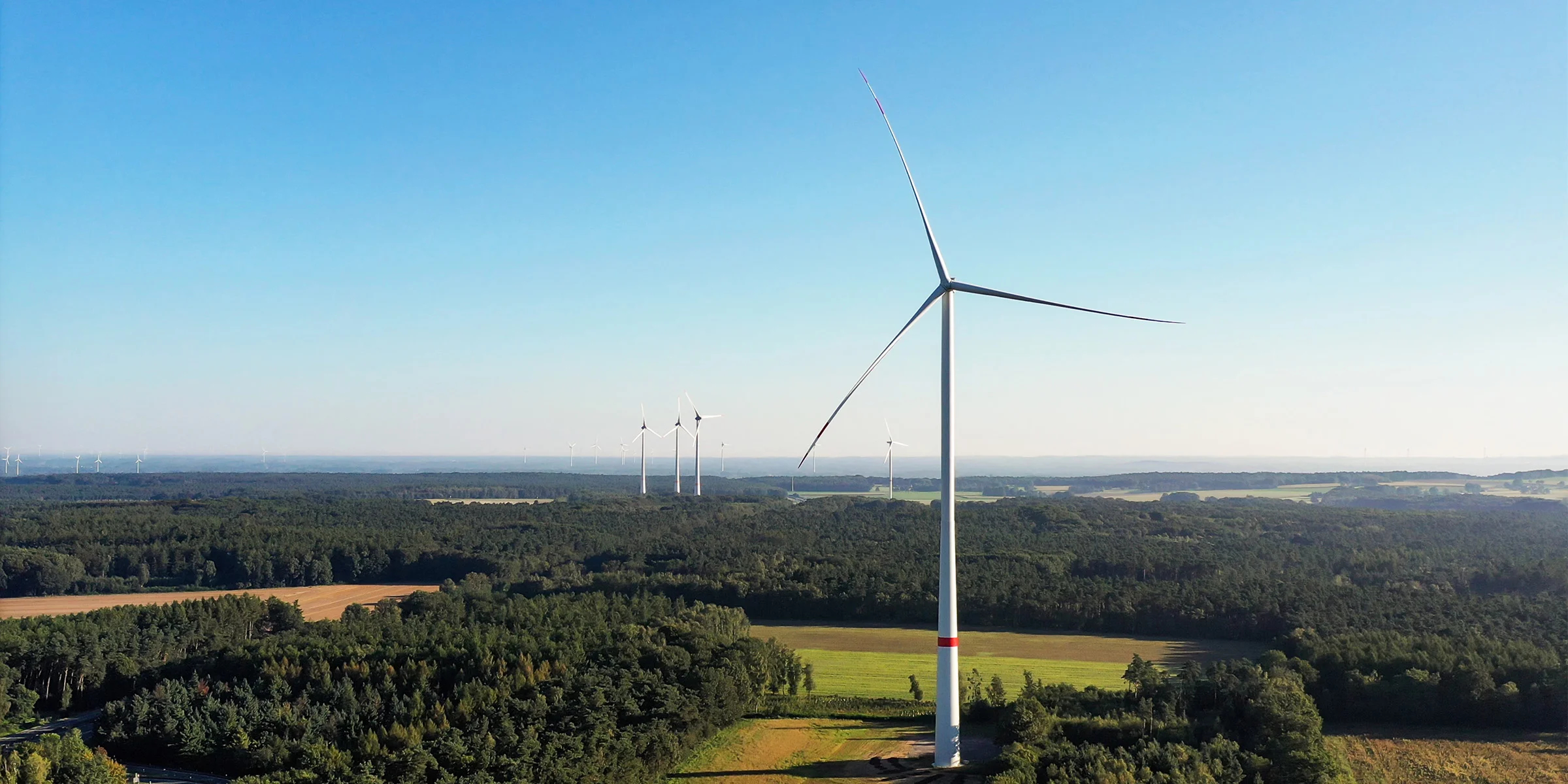 Das Bild zeigt eine Windturbine, die in einer weiten, grünen Landschaft steht.