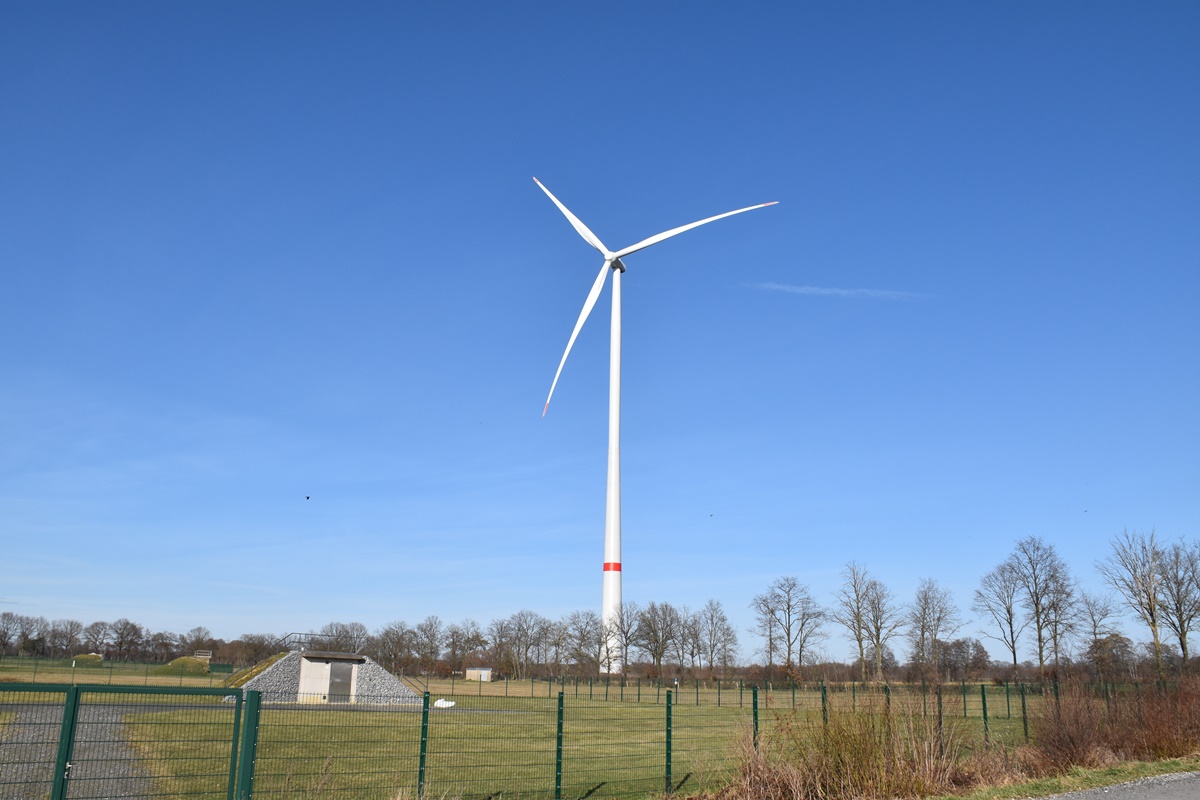 Windturbine in grüner Landschaft. Das Bild zeigt eine Windturbine auf einem offenen Feld unter einem klaren blauen Himmel.