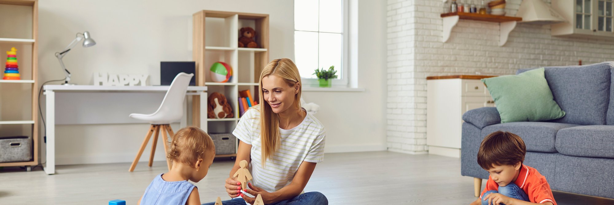 Mutter spielt mit Kindern im modernen Zimmer. Das Bild zeigt eine Mutter, die zusammen mit ihren zwei Kindern auf dem Boden eines hellen, modernen Zimmers spielt.