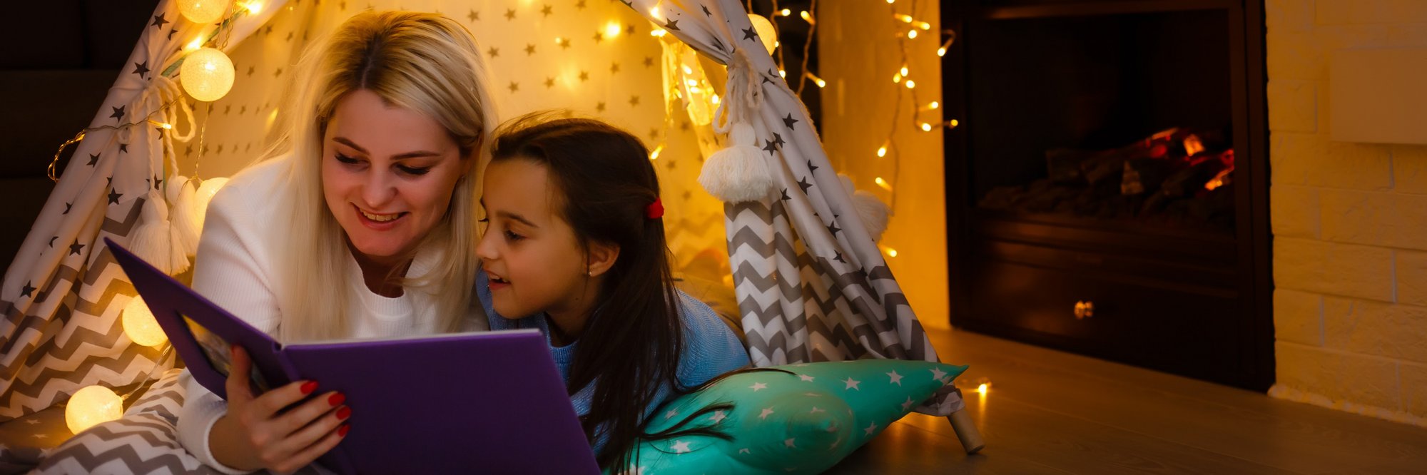 Mutter und Tochter lesen im Zelt. Mutter und Tochter, die zusammen in einem Zelt mit Lichtern ein Buch lesen.