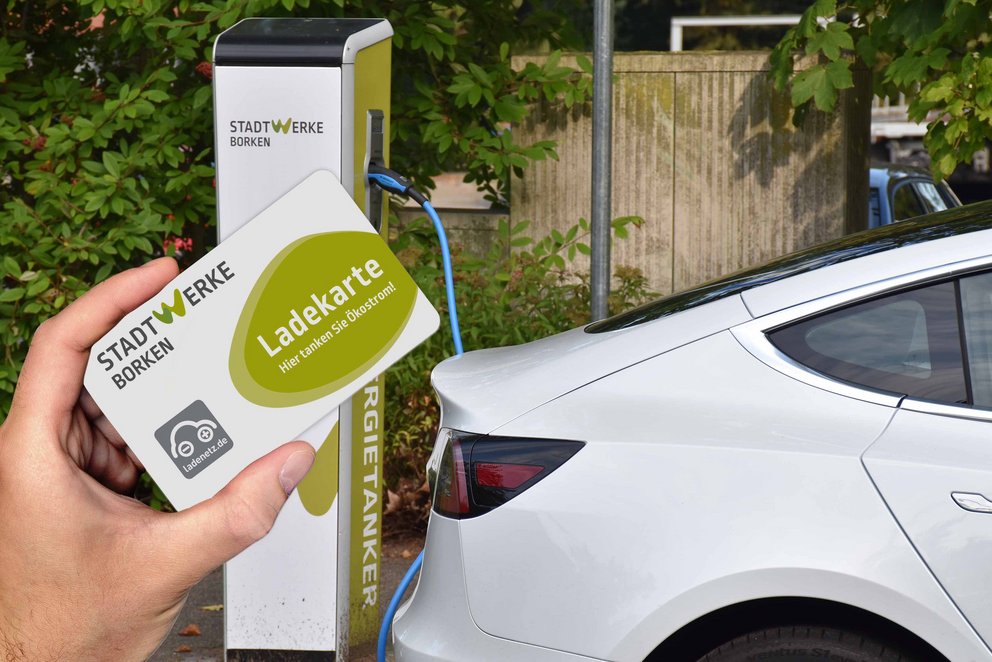 Person hält Ladekarte vor Elektroauto. Jemand hält eine Ladekarte in der Hand, während er sich einem Elektroauto nähert.