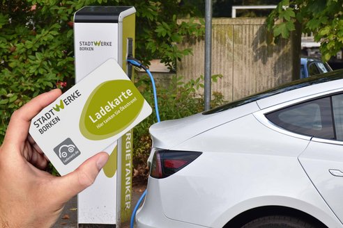 Person hält Ladekarte vor Elektroauto. Jemand hält eine Ladekarte in der Hand, während er sich einem Elektroauto nähert.