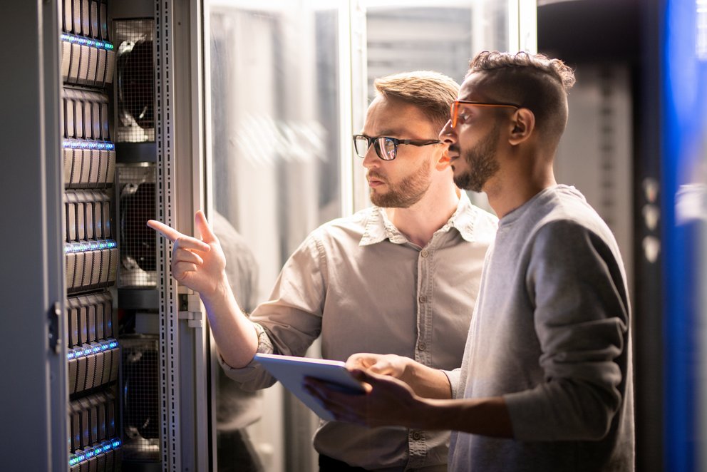 Personen arbeiten im Serverraum. Das Bild zeigt zwei Personen, die in einem Serverraum arbeiten und sich auf die Konfiguration oder Wartung von Servern konzentrieren.