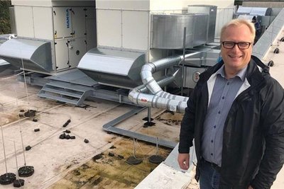 Das Bild zeigt eine Person auf einem Flachdach, umgeben von Lüftungsanlagen und Rohren.