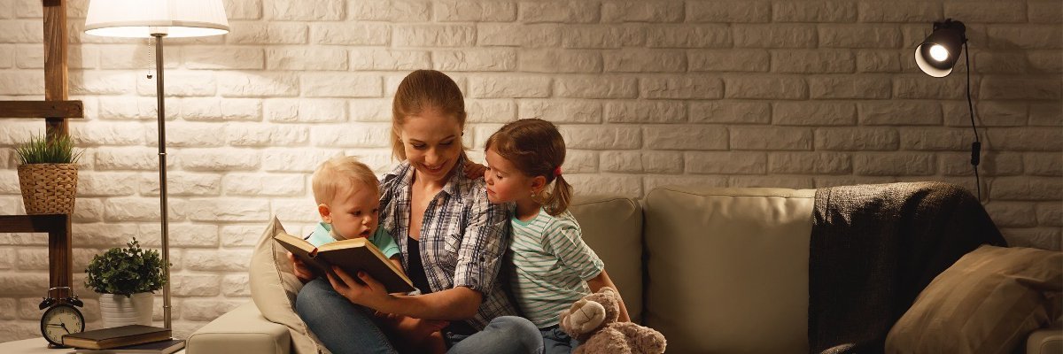 Mutter liest mit Kindern auf dem Sofa. Das Bild zeigt eine Mutter, die mit ihren Kindern auf dem Sofa ein Buch liest.