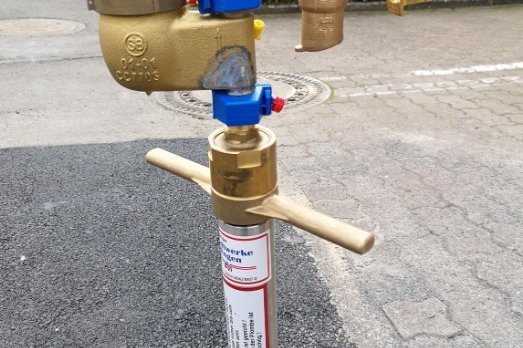 Wasserzähler und Ventile in Bodeninstallation. Das Bild zeigt einen Wasserzähler mit Anschlüssen, der in einem Bodenanschluss installiert ist.