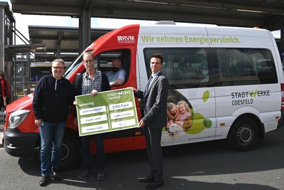  zwei Männer vor einem rot-weißen Kleinbus mit Werbeaufdruck, vermutlich bei einer symbolischen Übergabe oder Vorstellung