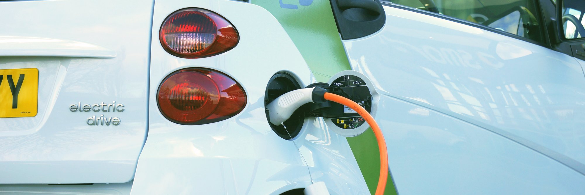 ein Elektroauto, das gerade aufgeladen wird, mit einem Ladeanschluss und einem Kabel, das an das Fahrzeug angeschlossen ist.