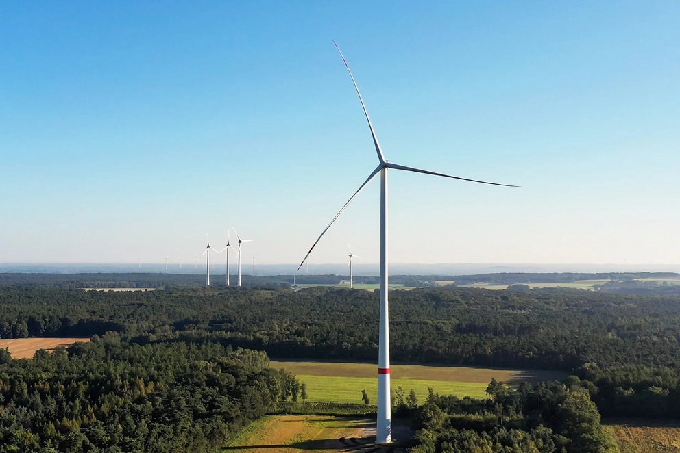 Das Bild zeigt eine Windturbine, die in einer weiten, grünen Landschaft steht.