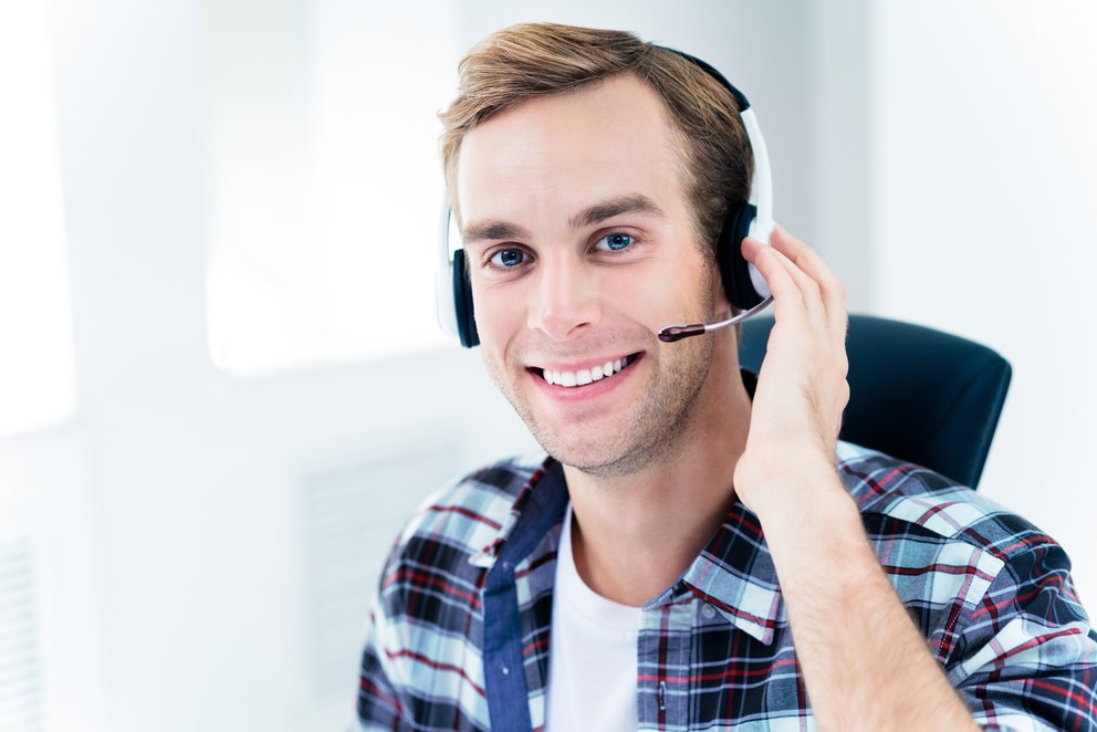 Mann arbeitet mit Headset am Computer Das Bild zeigt einen Mann, der mit einem Headset am Computer arbeitet und dabei lächelt.
