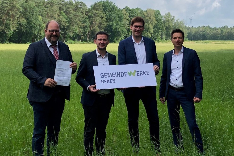 Gründung Gemeinde Werke Reken. Gruppe von vier Männer in Anzügen mit Firmenschild im Grünen.