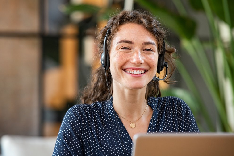 Eine lächelnde Frau mit Headset am Laptop. Eine lächelnde Frau mit Headset sitzt am Laptop.