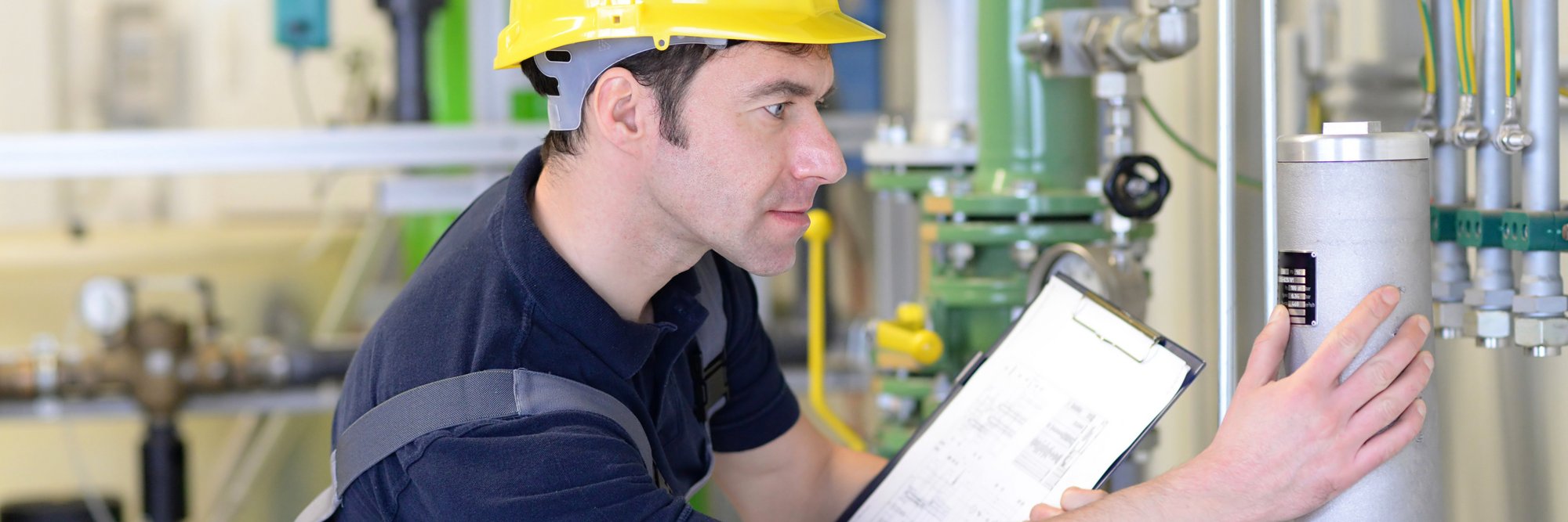 Mitarbeiter in Helm bei der Geräteprüfung. Mitarbeiter in Schutzkleidung und Helm, der ein technisches Gerät in einer industriellen Umgebung überprüft.