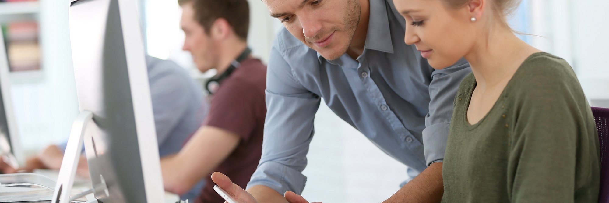 Personen arbeiten zusammen an einem Tisch, einer zeigt auf ein Tablet, während der andere darauf schaut.