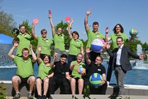 . Mehrere Menschen in grünen Shirts stehen zusammen und lächeln für ein Gruppenfoto.