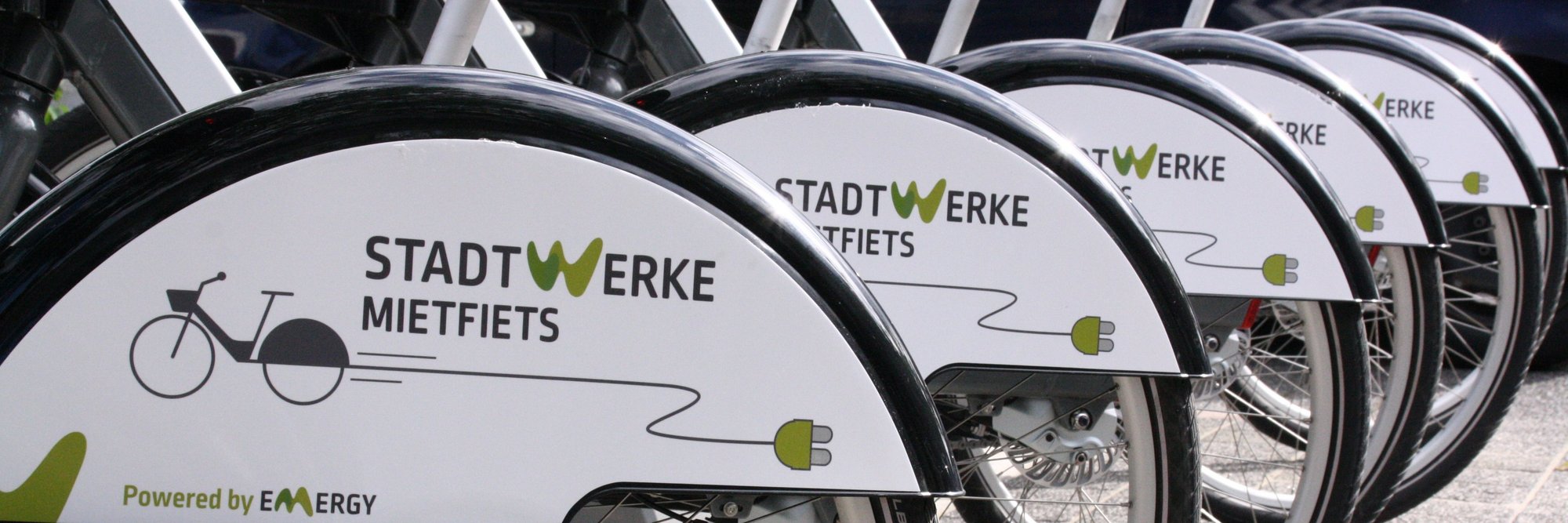 Stadtwerke-Fahrradverleih im öffentlichen Bereich. Eine Reihe von Fahrrädern, die Teil eines öffentlichen Verleihsystems zu sein scheinen, mit einem klar sichtbaren "Stadtwerke" Logo.