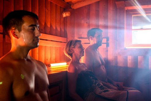 Saunaraum mit Gästen. Eine Gruppe von Menschen entspannt in einem Saunaraum, umgeben von Holzverkleidung und dampfender Luft.