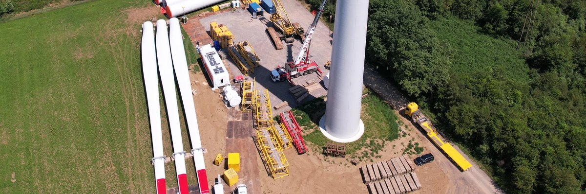 Aufbau eines Windkraftwerks, mit einer Windturbine und den Bauteilen in der Nähe, die für die Montage bereitgestellt werden.