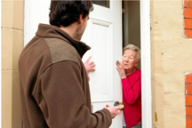 Handwerker, der an der Tür einer älteren Dame steht und mit ihr spricht.