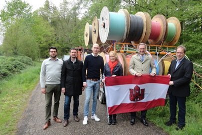 N. Waning, T. Abels, P. Nettels, M. Schulze Hessing, M. Hilkenbach, B. Rose mit Stadtfahne vor Glasfaserrohren