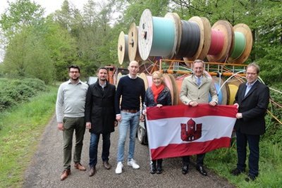 N. Waning, T. Abels, P. Nettels, M. Schulze Hessing, M. Hilkenbach, B. Rose mit Stadtfahne vor Glasfaserrohren