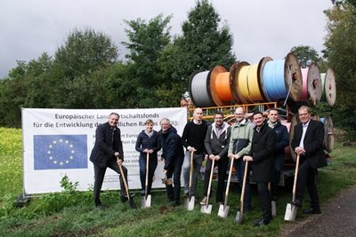 Vertreter der Beteiligten mit Spaten vor Leerrohr-Trommeln