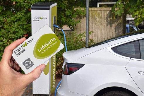 Jemand hält eine Ladekarte in der Hand, während er sich einem Elektroauto nähert.