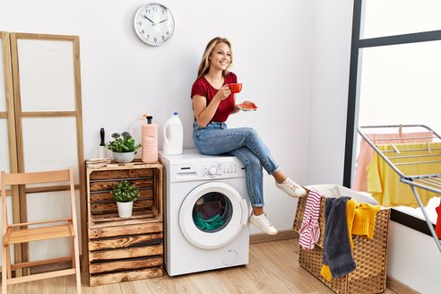 Frau sitzt auf Waschmaschine