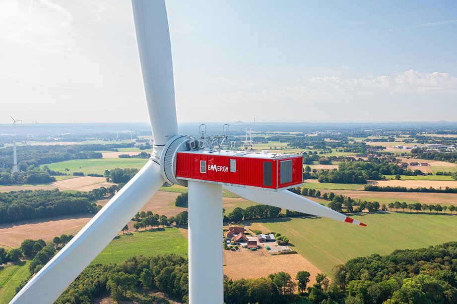Das Bild zeigt eine Windkraftanlage (WKA) aus der Drohnenperspektive. Auf der Gondel steht das Logo der Emergy.