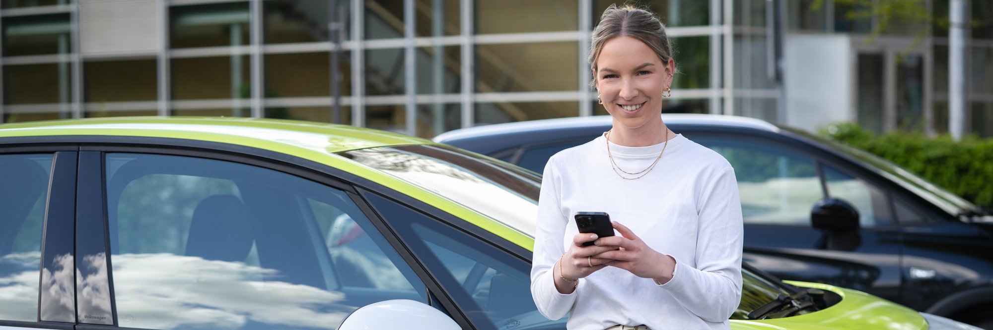 Frau steht mit Handy am Auto angelehnt