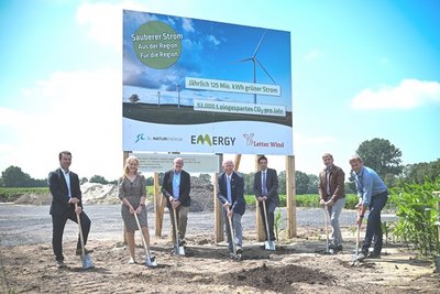 eine Gruppe von Personen, die ein Baustellenbanner für ein Windkraftprojekt präsentieren.
